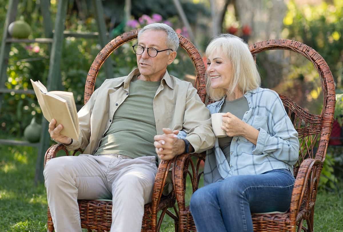 Loving Elderly Couple Reading Book Together, Sitting In Wicker C